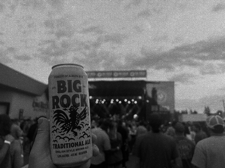 A Traditional Ale can held in front of the Barn Burner 2025 stage and crowd at Big Rock Brewery.